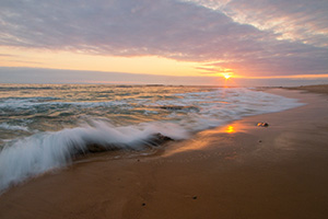 Waves of the Pacific crash on the shore of Crystal Cove State Park in California while the sun sets in the distance. - California Landscape Photograph