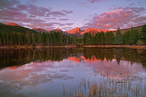 During a cool October sunrise, bright with alpenglow, the peaks of the continental divide, Powell Peak, Taylor Peak, Otis Peak, Hallett Peak, and Flattop Mountain are reflected in the calm waters of Sprague lake while underlit clouds hover overhead. - Colorado Photograph
