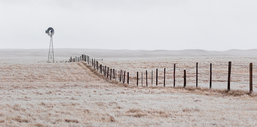 Scenic landscape panoramic photograph of a windmill and a fence in the winter at Oglala National Grasslands. - Nebraska Photography