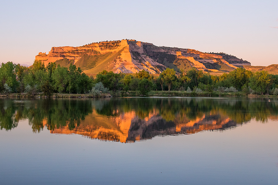 Glowing in the light of the recently risen sun, Scotts Bluff National Monument in western Nebraska is reflected in a small nearby lake. - Nebraska Photography