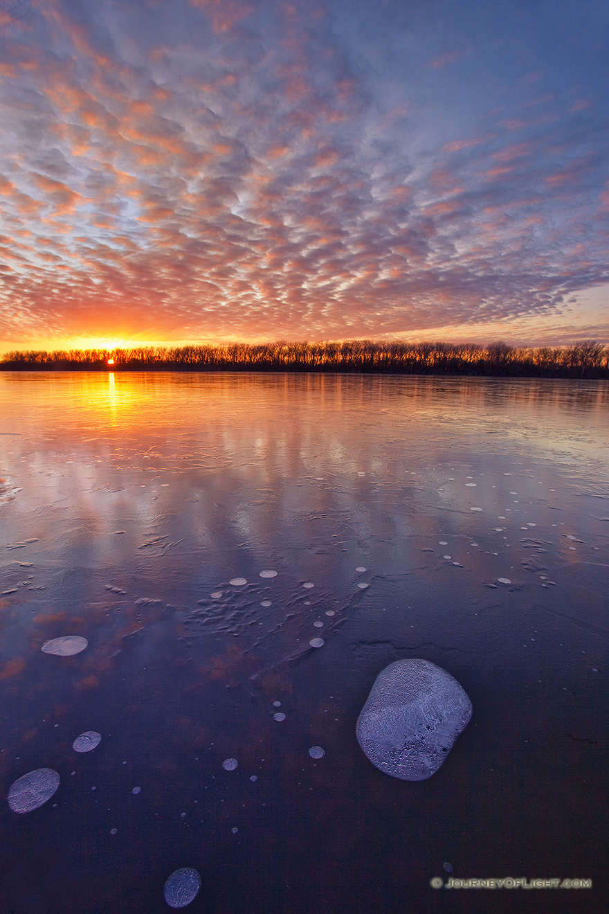 The warm setting sun shines brightly across the frozen lake on a chilly January evening before dipping below the horizon. - DeSoto Picture