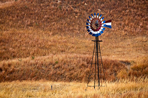 A scenic landscape photograph of a windmill painted red, white, and blue in the sandhills of Nebraska. - Nebraska Photograph