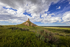 On a cool spring day, under a beautiful blue sky filled with puffy white clouds, Chimney Rock glows in the warm light of the afternoon sun. - Nebraska Photograph
