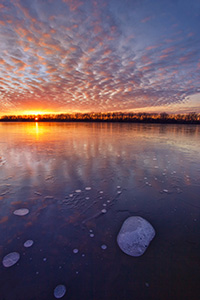 The warm setting sun shines brightly across the frozen lake on a chilly January evening before dipping below the horizon. - Nebraska Landscape Photograph
