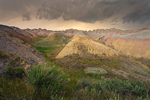 As a storm passes over Badlands National Park in South Dakota, the last light of the day illuminates a few distant clouds. - South Dakota Photograph