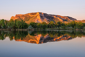 Glowing in the light of the recently risen sun, Scotts Bluff National Monument in western Nebraska is reflected in a small nearby lake. - Nebraska Photograph
