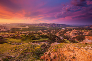 Above a bend in the Little Missouri River in the North Unit of Theodore Roosevelt National Park, clouds glow purple and orange as the sun just begins to rise above the horizon. - North Dakota Landscape Photograph