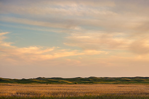 The last light of sunset skims across the Nebraska Sandhills and casts a warm glow on the clouds above. - Nebraska Photograph